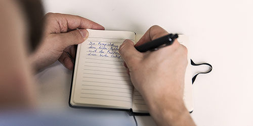 Jemand schreibt mit einem Stift in ein kleines Notizbuch