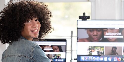 lächelnde Person, die sich umdreht, vor zwei Computerbildschirmen